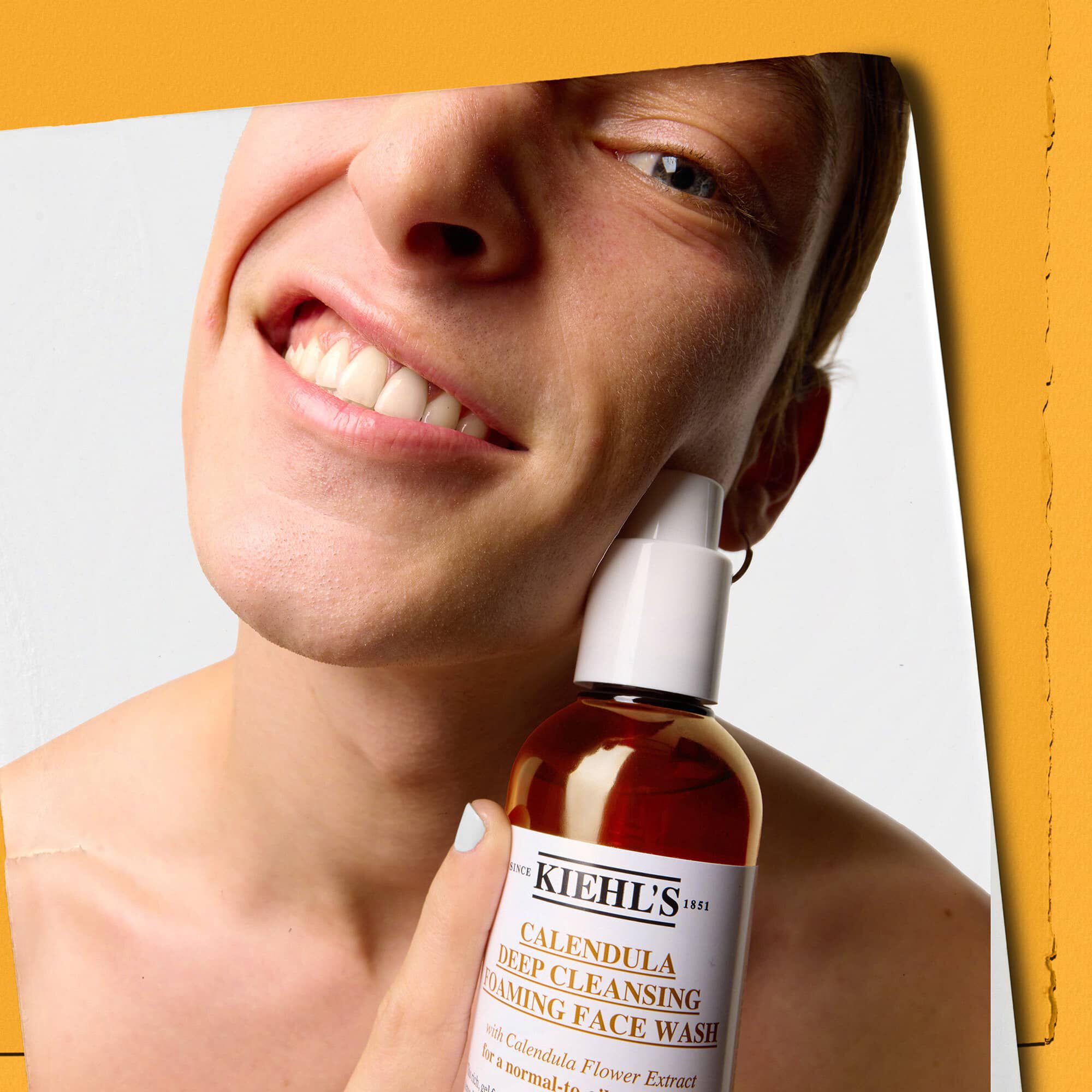 Model care ține un flacon de gel de curățare facială Kiehl's Calendula Deep Cleaning Foaming Face Wash