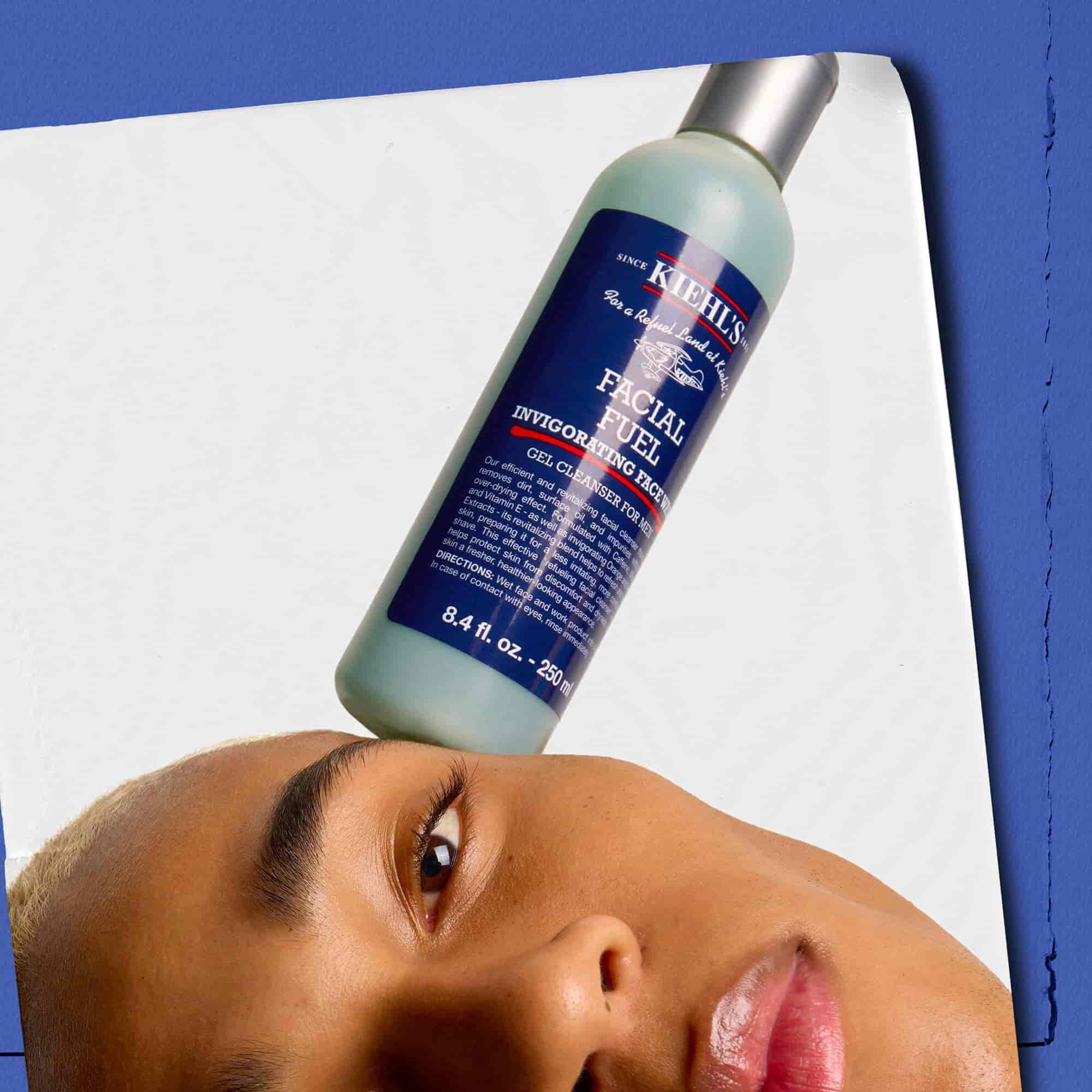 Model care ține un flacon de gel de curățare Kiehl's Facial Fuel Energizing Face Wash in echilibru pe față