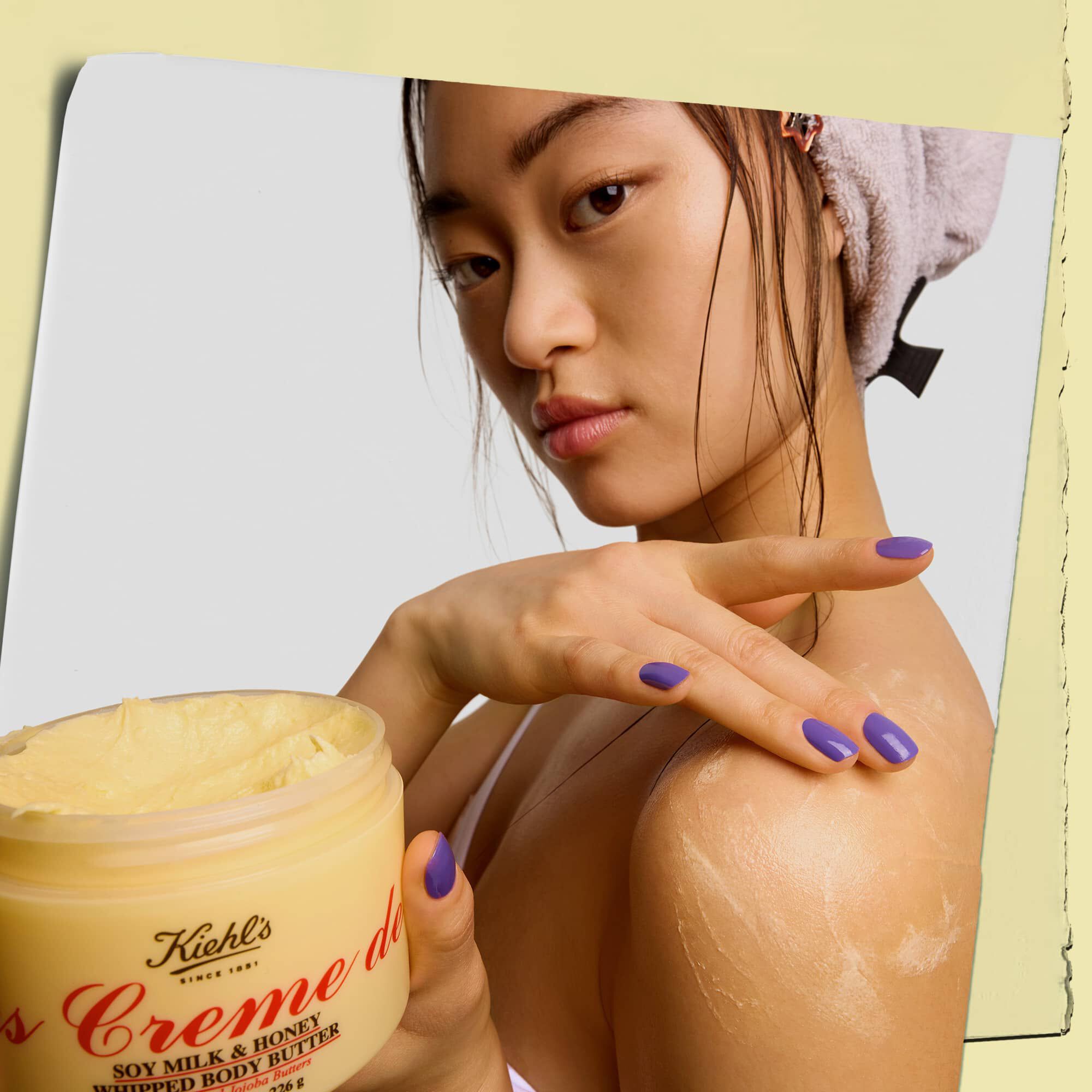 Model care ține un borcan și aplică unt de corp Kiehl's Creme de Corps Whipped Butter