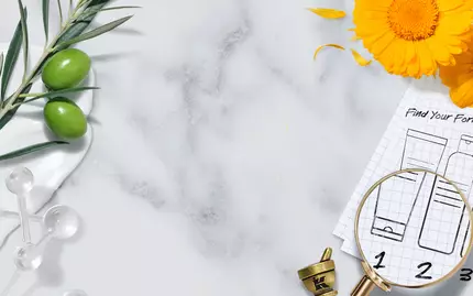 A flat lay featuring a marble surface with botanical elements like olive branches and marigold petals, along with a mortar and pestle. There's a magnifying glass over a grid paper with markings of product formulas, and a decorative border with space for text.