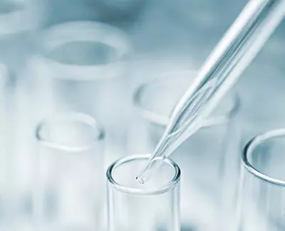 A close-up of a pipette above a test tube, illustrating a laboratory setting focused on scientific experimentation.