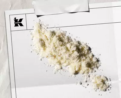 Pudră alb-gălbuie reprezentand fulgi de ovăz coloidal 1% pe o cearșafură albă cu un logo negru Kiehl's in colț.