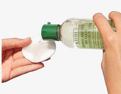 Flacon de loțiune curățare Kiehl's cu dispenser verde, turnandu-se pe un disc demachiant.
