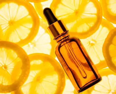A dropper bottle of amber glass is placed on a background of bright yellow lemon slices, creating a fresh and vibrant aesthetic.