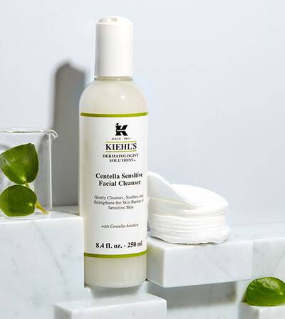 Flacon de cleanser facial Kiehl's Centella Sensitive pe un suport de marmură, alături de dischete demachiante.