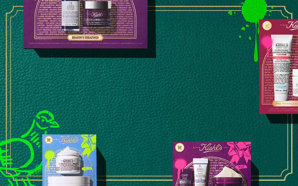Horizontal banner with a dark green textured background and gold border lines, featuring colorful Kiehl’s gift boxes in pink, blue, and purple, each displaying skincare products. Green artistic accents appear on both sides.