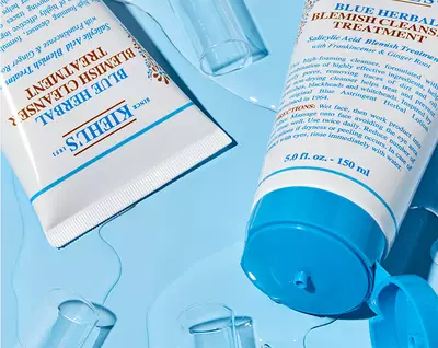 Produse de ingrijire a pielii Kiehl's, amplasate pe un fundal albastru, evidențiind textura și ambalajul.