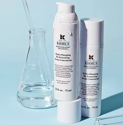 Flacoane de ser pentru re-texturizare Kiehl's, pe fundal albastru, alături de un cilindru gradat.