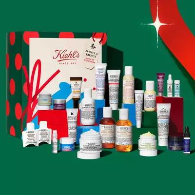 Calendarul de advent de sărbători și setul de cadouri pentru ingrijirea pielii Kiehl's, care conține diverse creme, serumuri, produse de curățare și tratamente intr-un decor festiv.