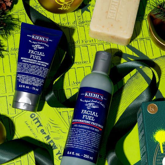 Kiehl’s Facial Fuel cleanser and moisturizer arranged with a bar soap and green holiday decorations on a bright yellow background.