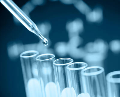 A close-up of a pipette dropping a liquid into a set of test tubes, with a blurred background featuring a DNA structure.
